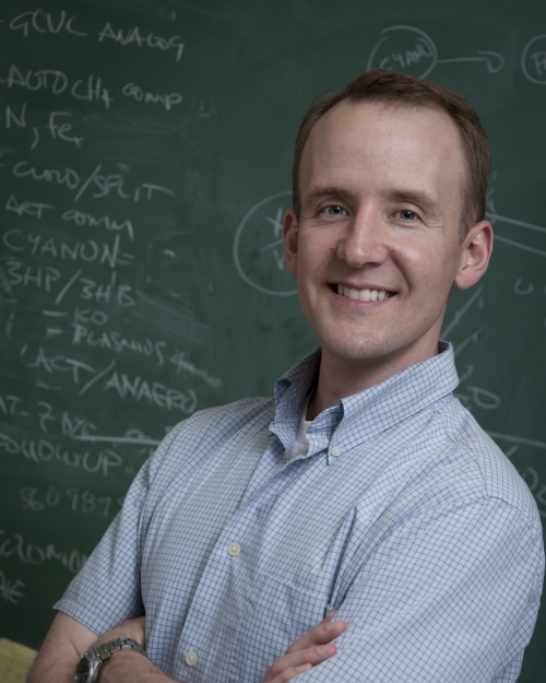 man in a collar shirt standing in front of a chalkboard