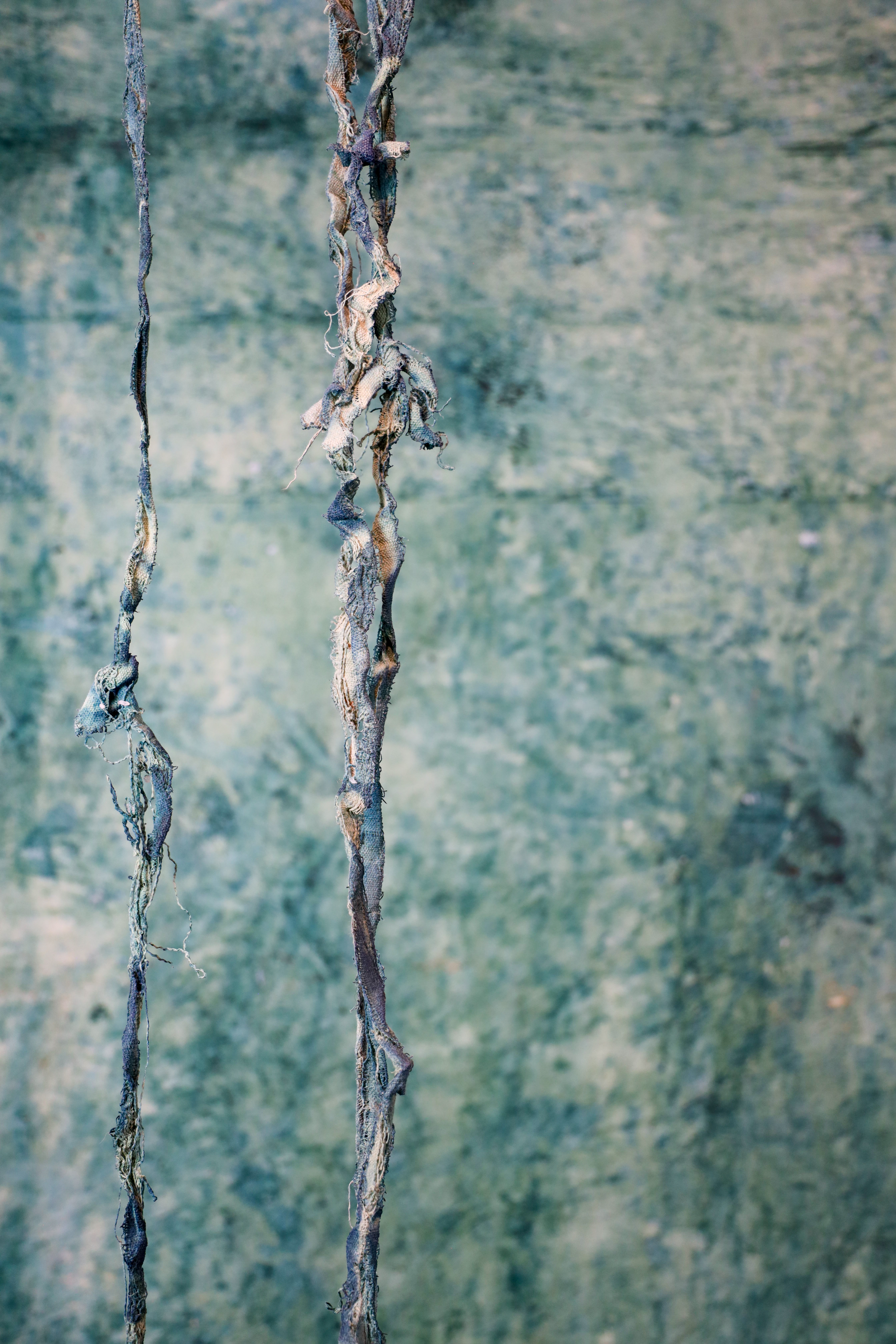 A blue and tan frayed piece of fabric in front greenish blue backgroundof a 