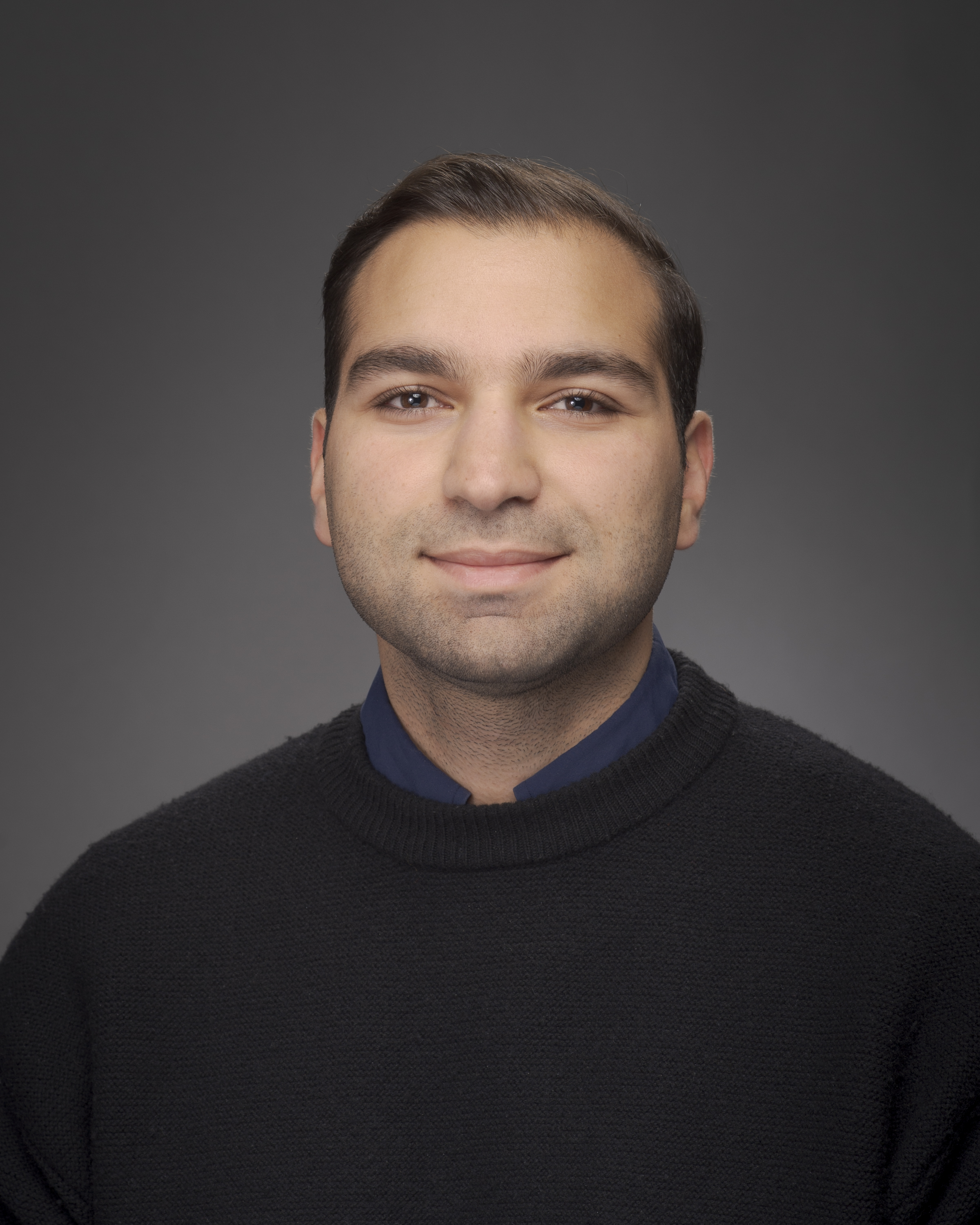 A portrait of a person with short dark hair and light facial hair wearing a black shirt